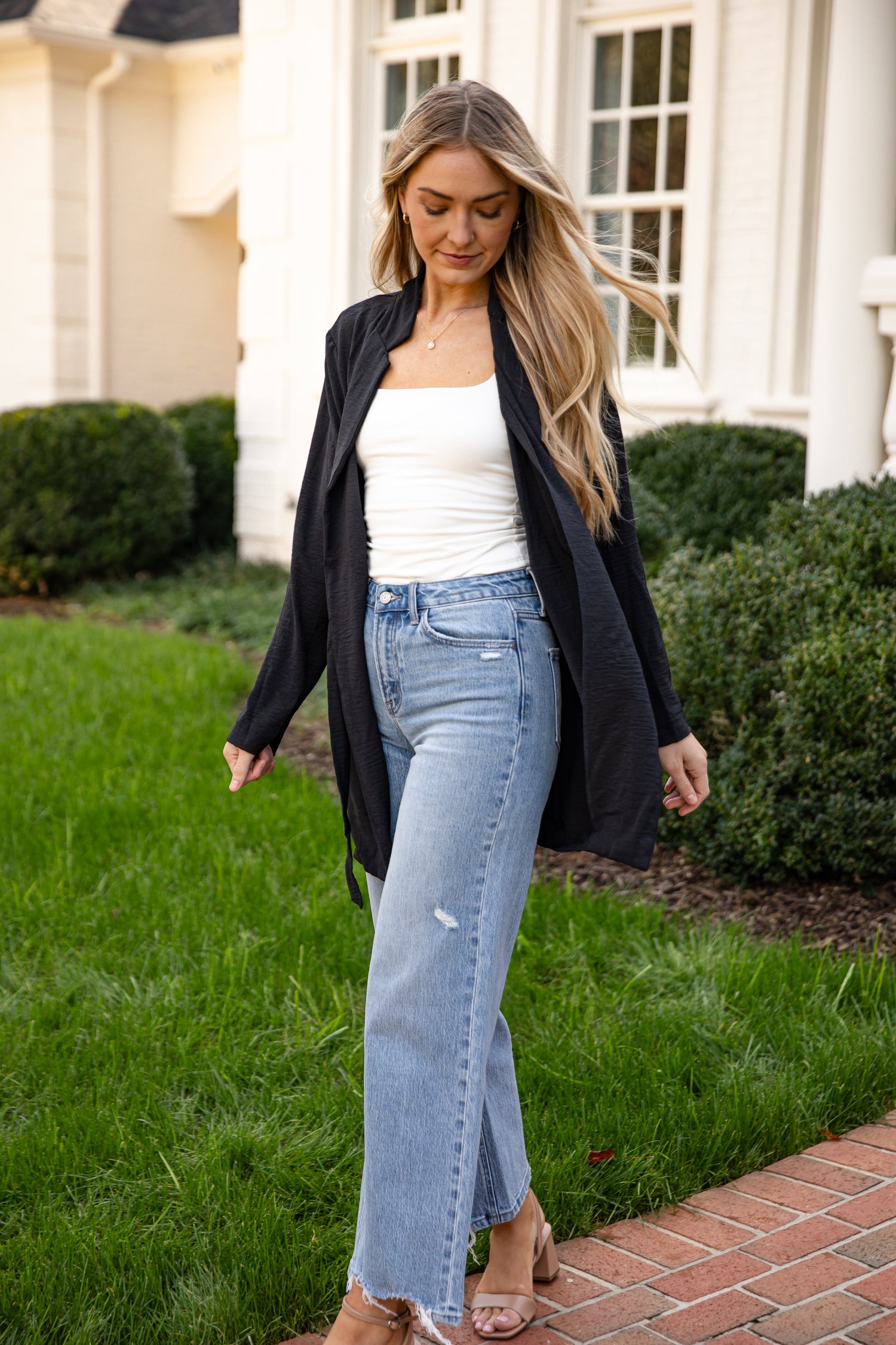 Woman in a white top and blue jeans standing on a grassy area with a building in the background
