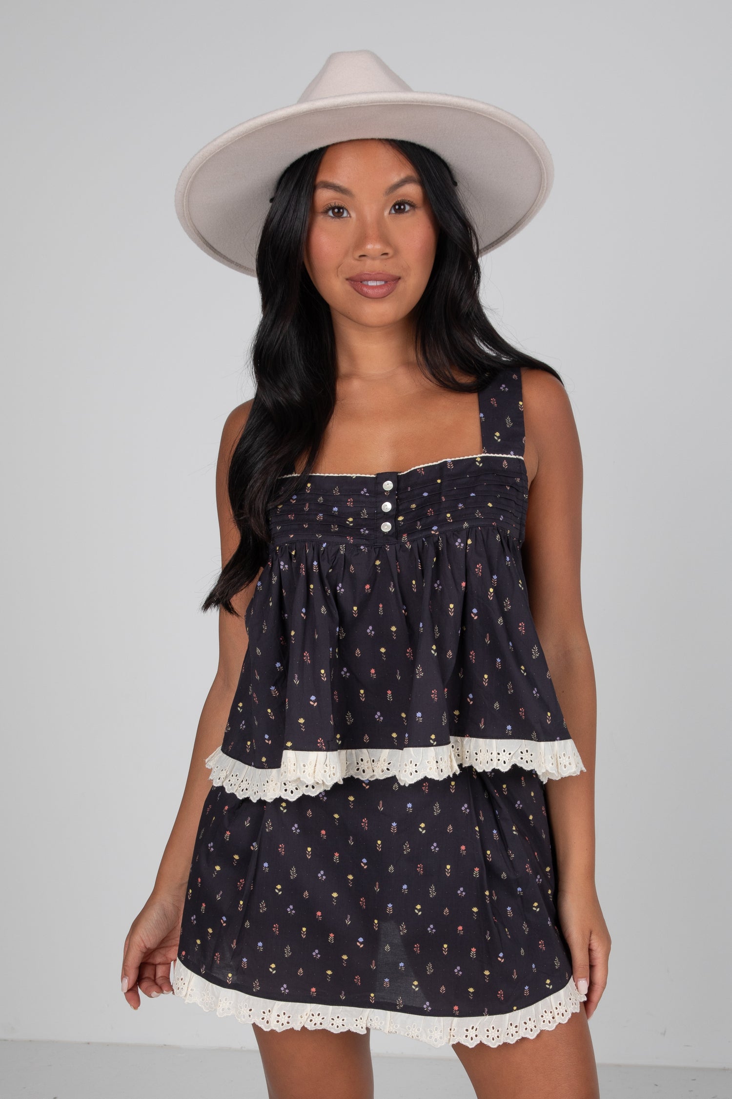 Woman wearing a navy dress with white lace trim and a white hat on a gray background