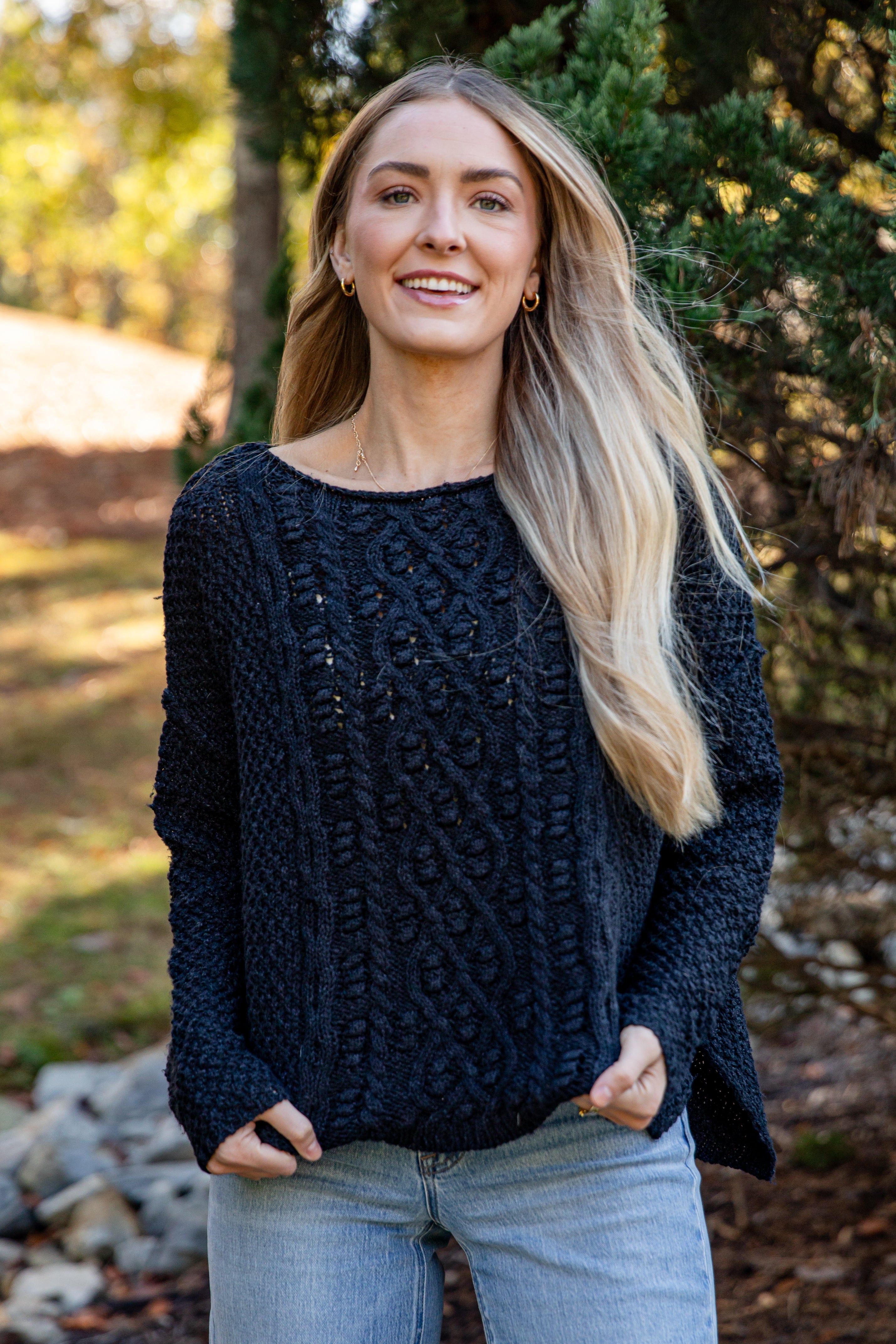 Woman wearing a dark blue knitted sweater outdoors with trees and rocks in the background