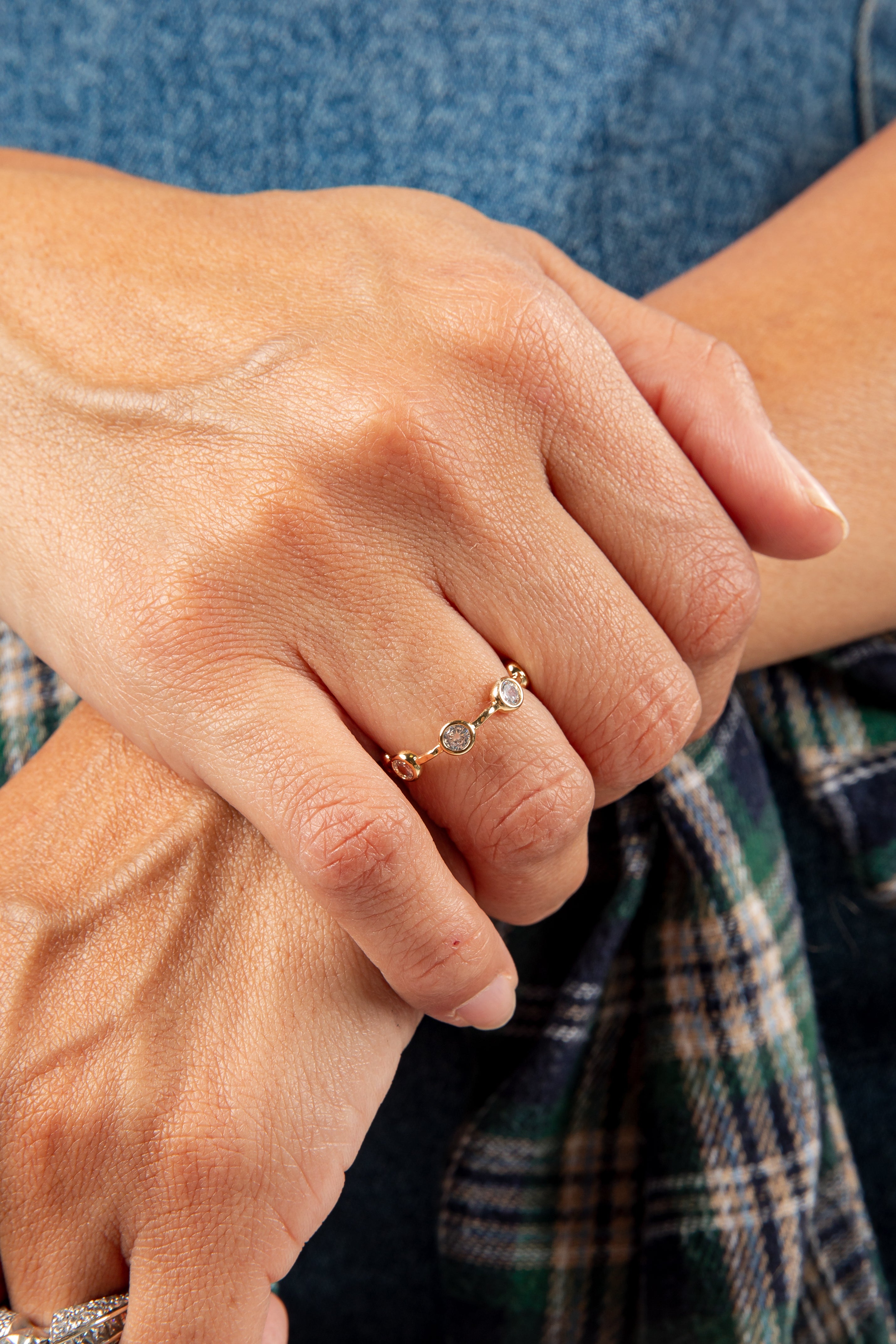 Close-up of a hand wearing a gold ring with a diamond on a blue denim background