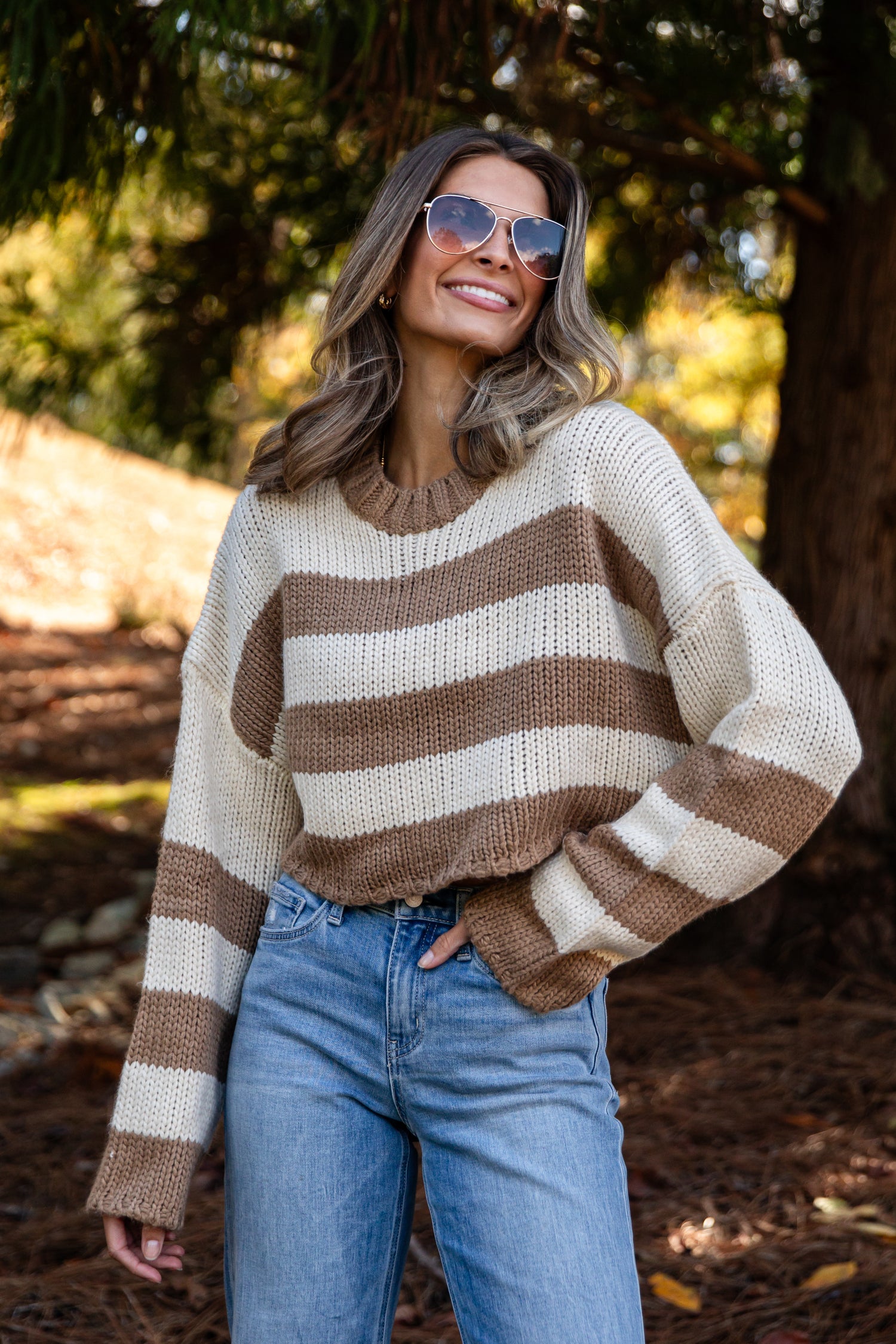 Woman wearing a striped sweater and sunglasses in a forest setting