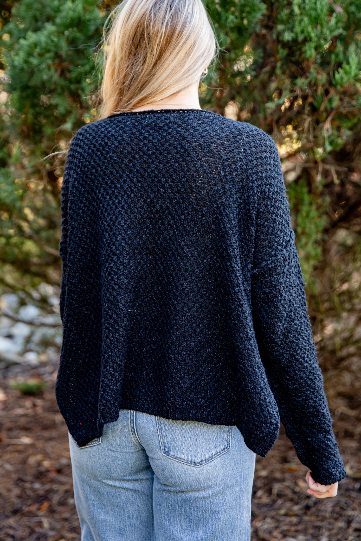 Person wearing a dark blue knitted sweater in a forest setting