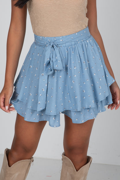 Person wearing a blue floral skirt with beige boots on a plain background