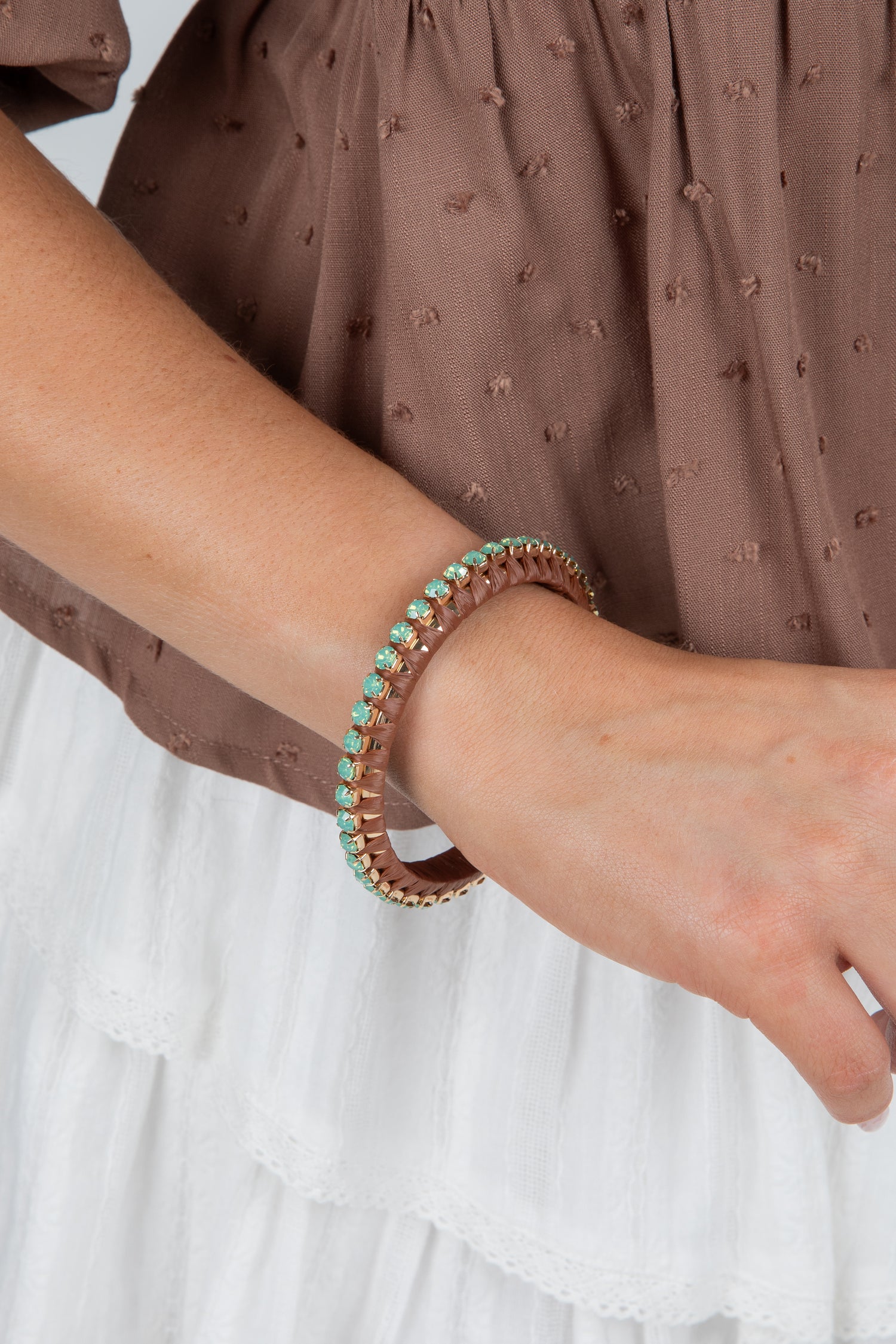 Close-up of a wrist wearing two bracelets with a brown top and white background
