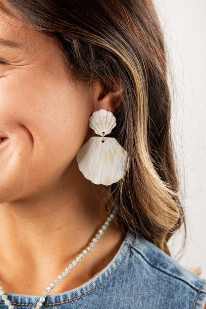 Close-up of a person wearing white shell earrings with a blurred background