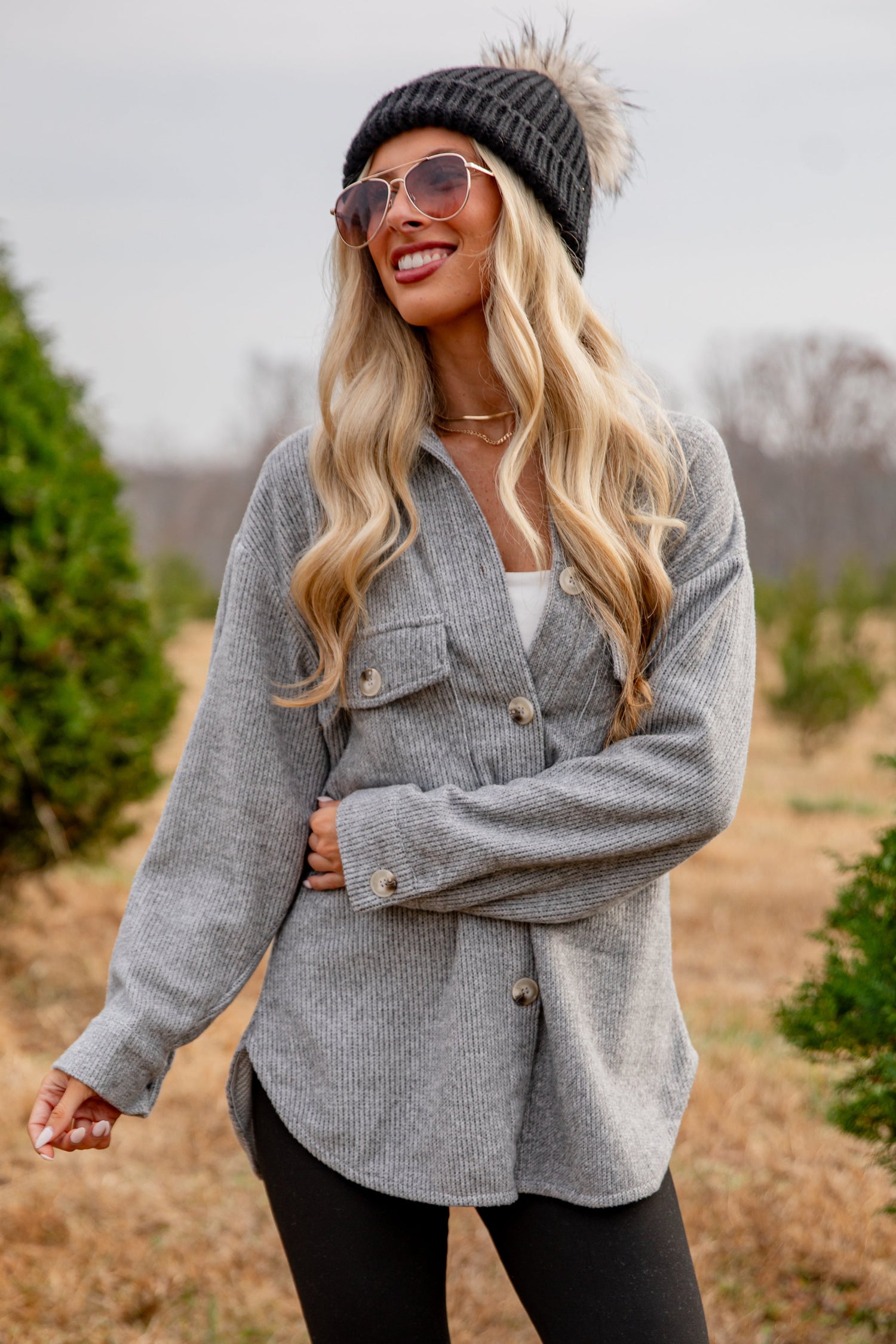 Woman wearing a gray jacket and black beanie in a field with trees in the background