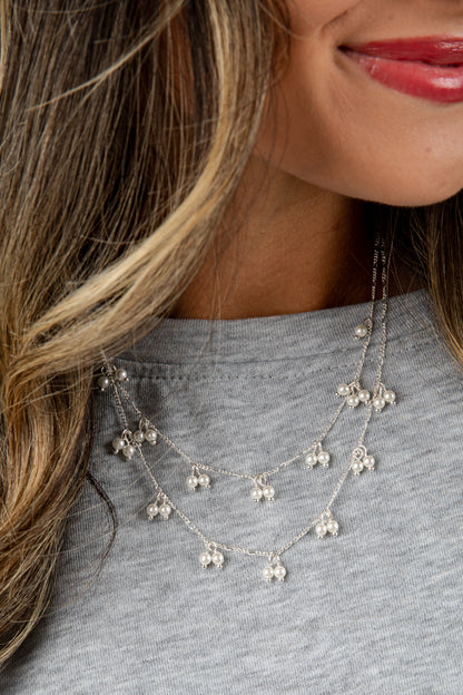Silver necklace with floral pendants worn by a person with long hair and red lipstick.