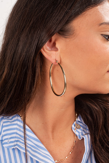 Close-up of a person wearing gold hoop earrings and a blue striped shirt.