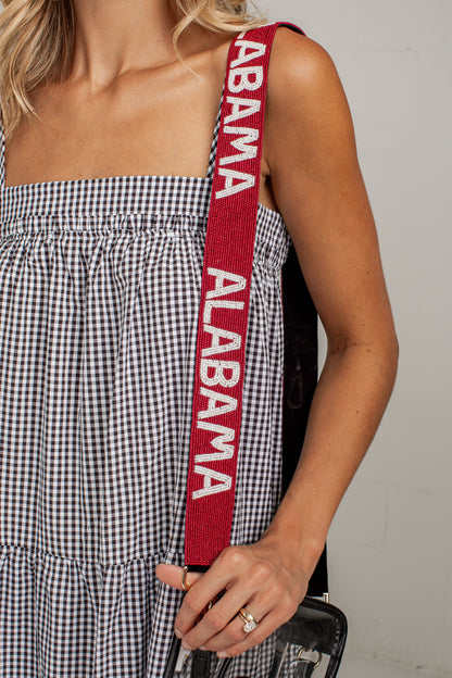 Close-up of a woman wearing a black and white gingham dress and holding a red shoulder strap with &