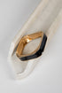 A gold-toned metal cuff bracelet with a wide, curved black enamel inlay, displayed on a white marble prop against a light gray background.