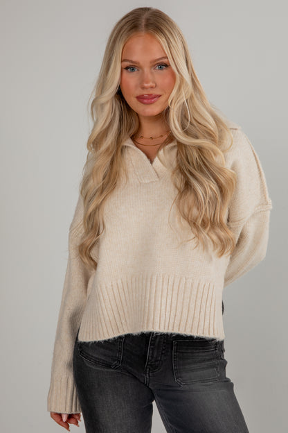 Woman wearing a beige sweater and black pants against a gray background