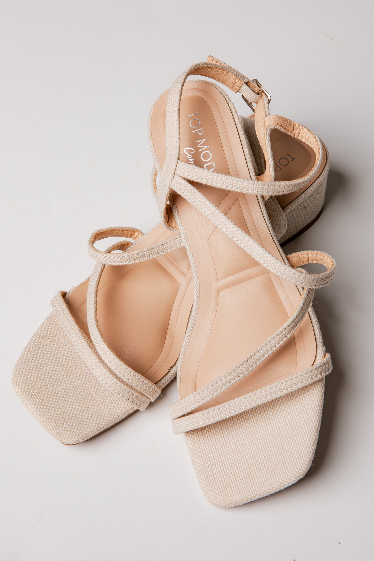 Pair of beige strappy sandals on a light gray background