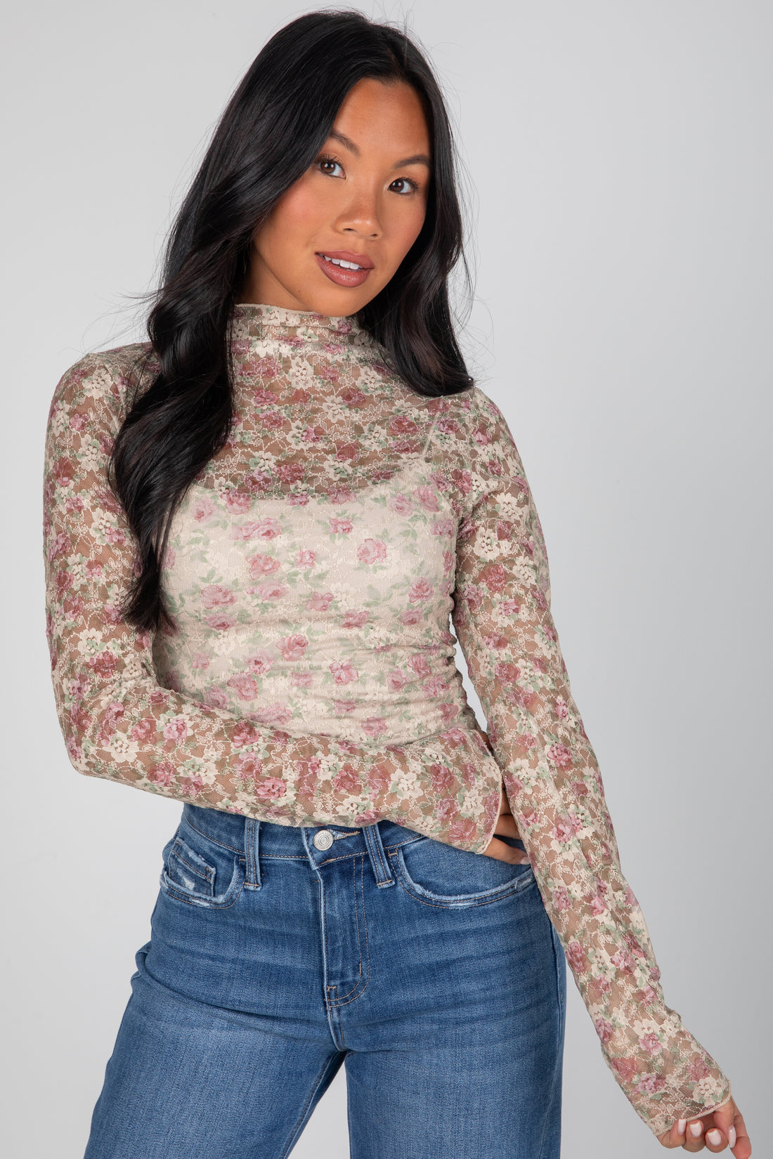 Woman wearing a floral long-sleeve top and blue jeans against a gray background
