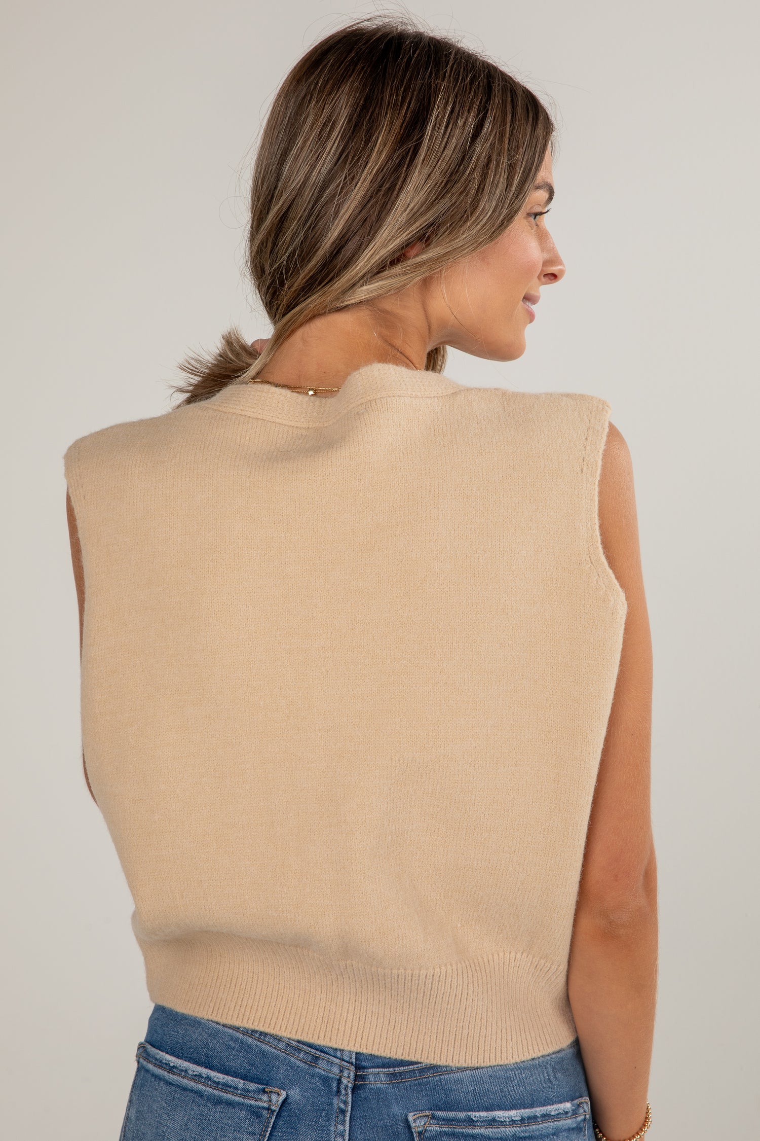 Woman wearing a beige sleeveless sweater against a plain background