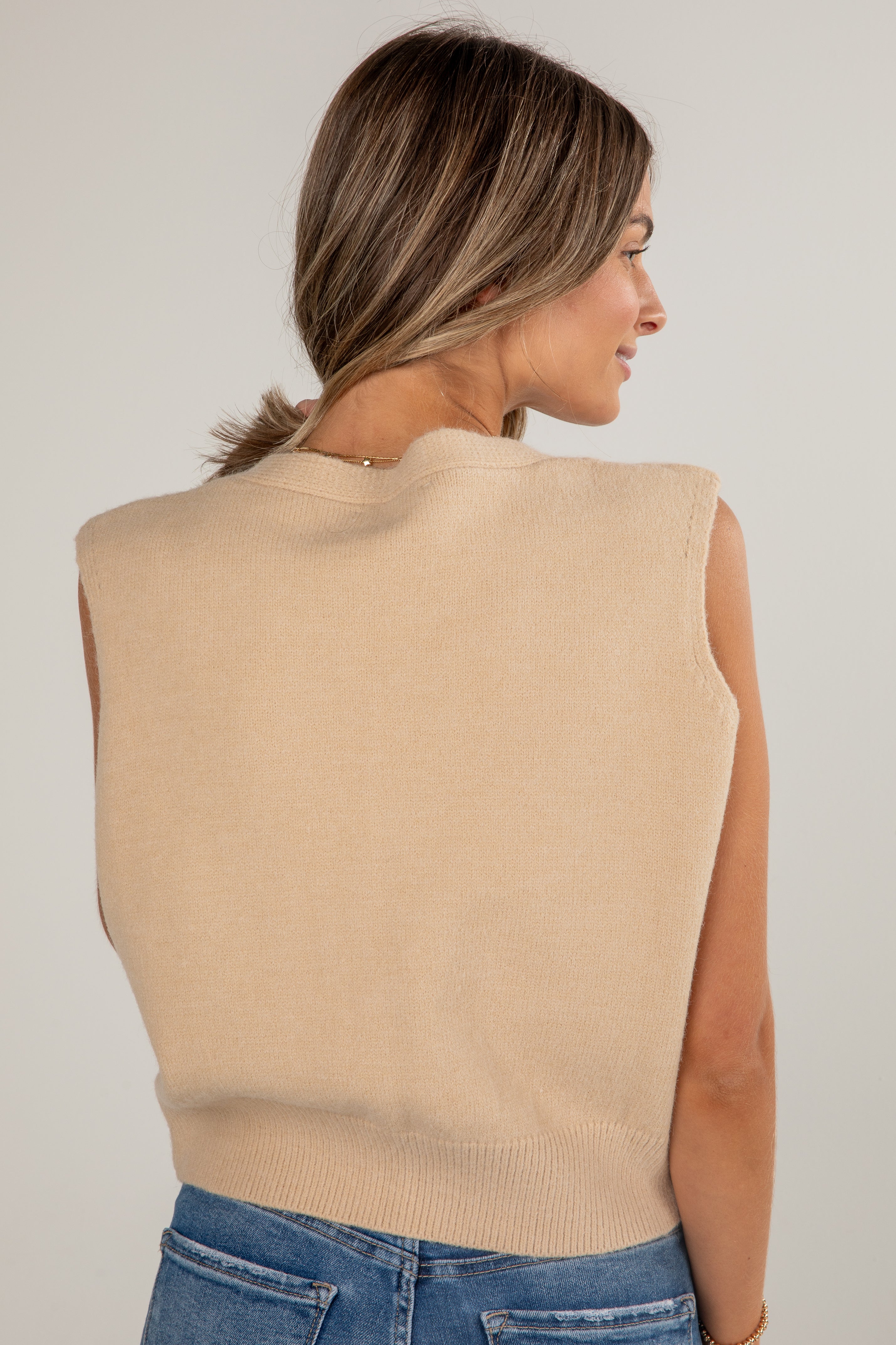 Woman wearing a beige sleeveless sweater against a plain background