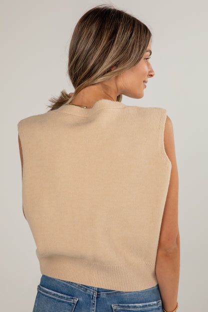 Woman wearing a beige sleeveless sweater against a plain background