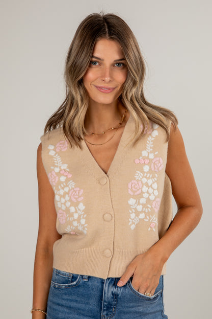 Woman wearing a beige cardigan with floral embroidery on a plain background
