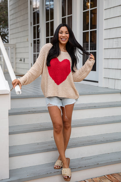 Woman wearing a beige sweater with a red heart design on a staircase.