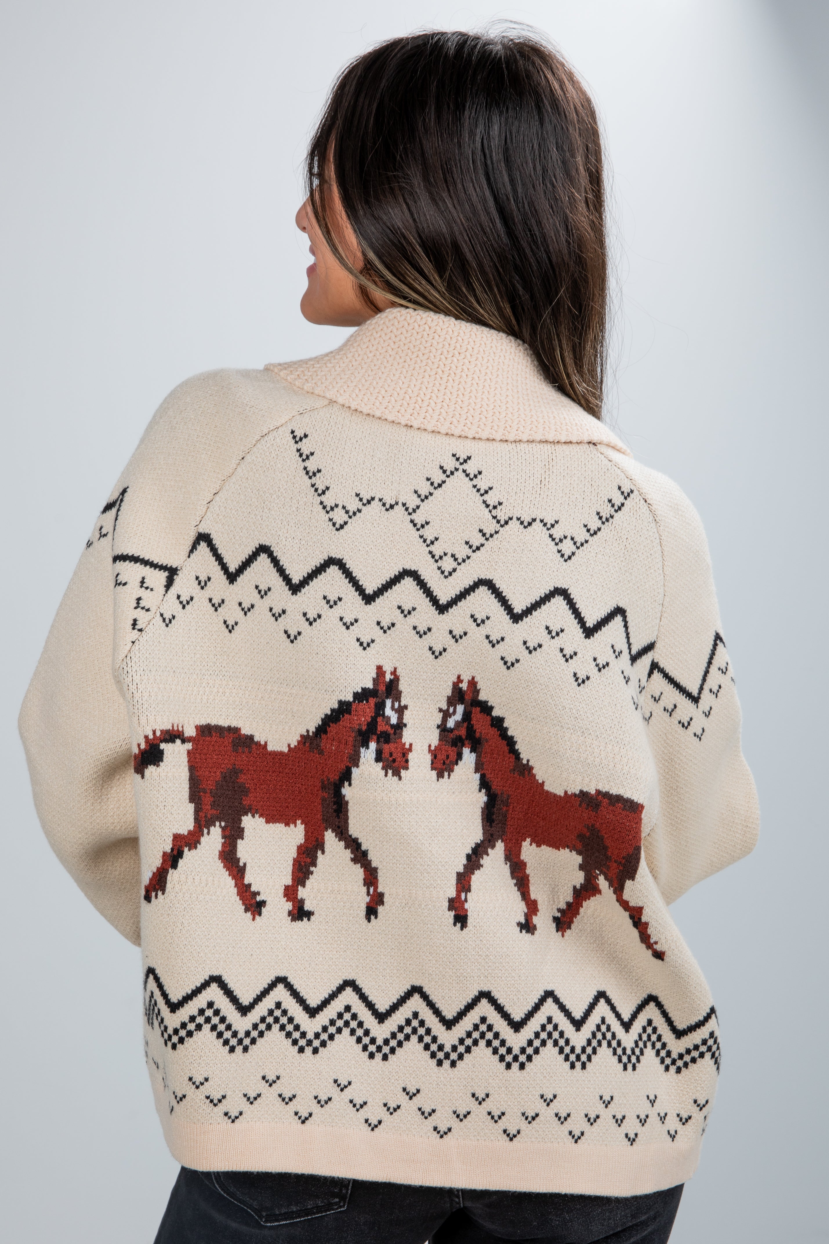 Person wearing a cream-colored sweater with horse designs and patterns on a light gray background
