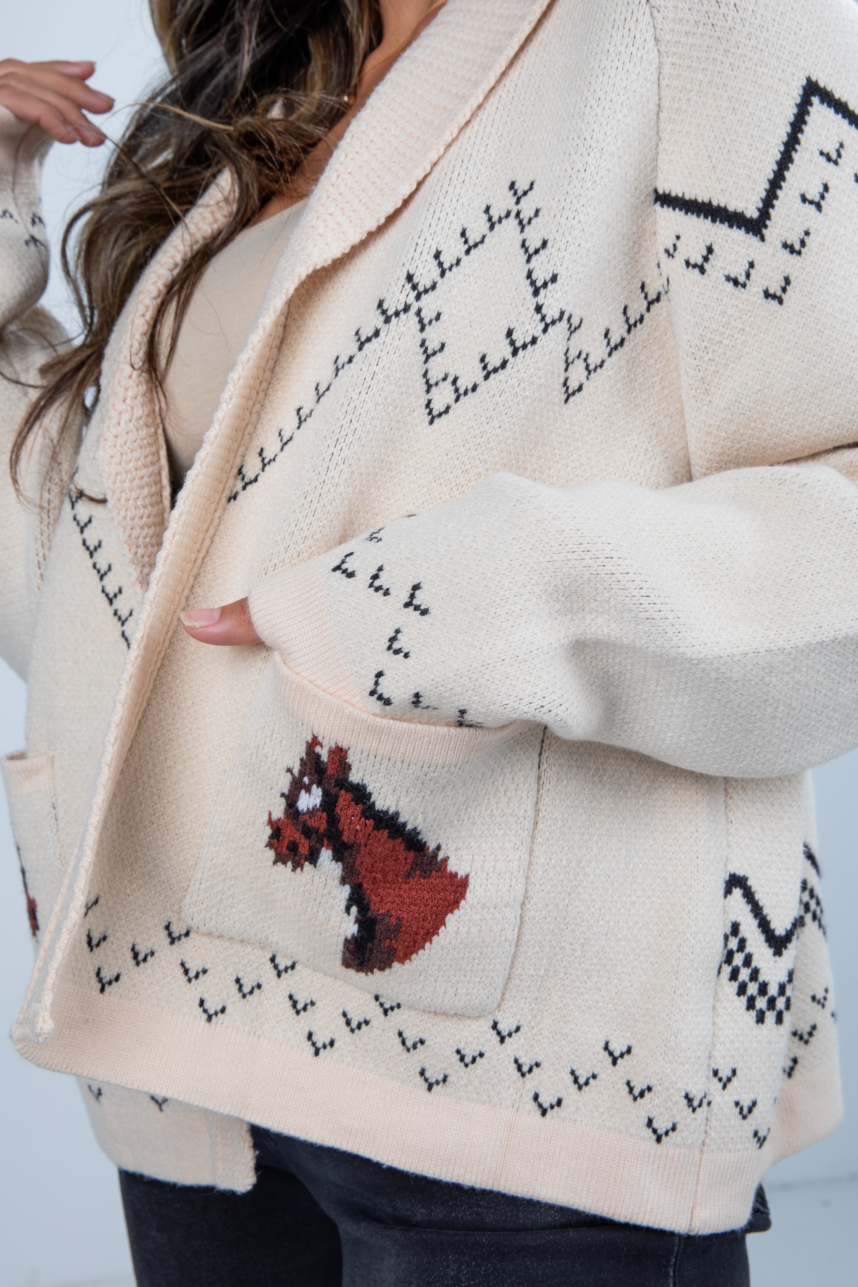 Close-up of a cream-colored cardigan with black geometric patterns and a red design on a light background.