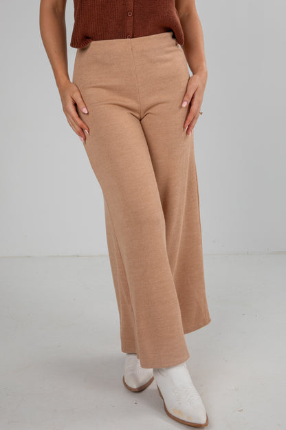 Person wearing tan pants and a brown top on a plain background