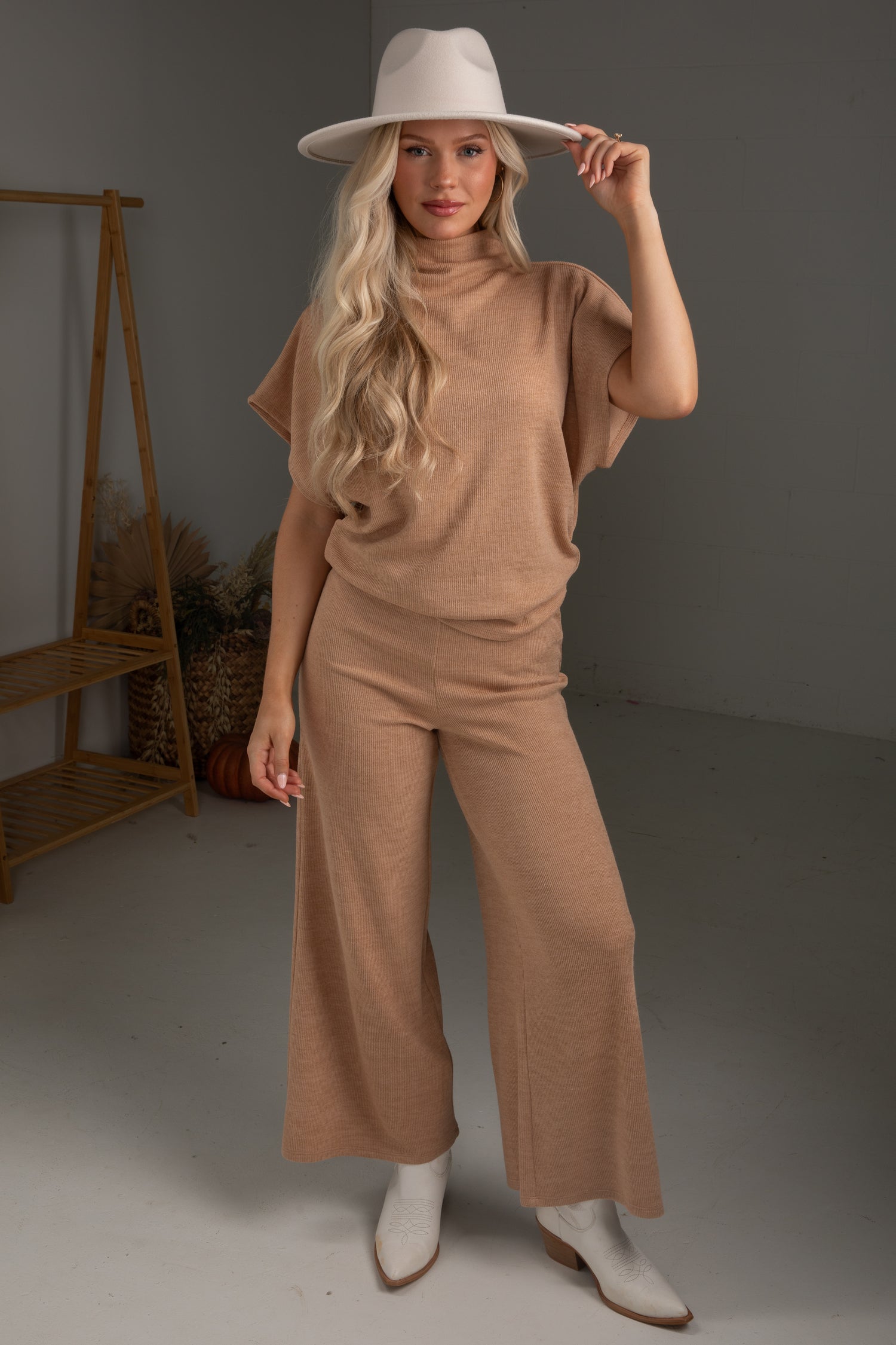 Woman wearing a brown outfit with a white hat in a studio setting