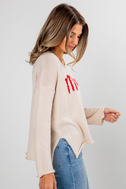 Woman wearing a beige sweater with red text and blue jeans on a light gray background