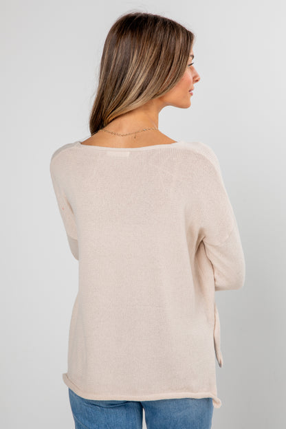 Woman wearing a beige sweater and blue jeans on a plain background