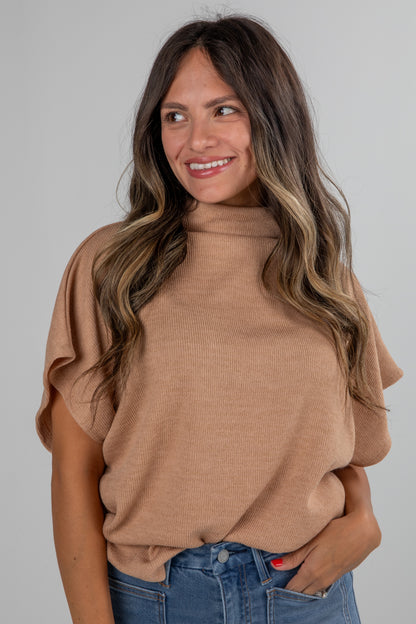 Woman wearing a brown sweater and blue jeans against a gray background