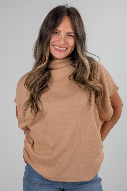 Woman wearing a beige sweater and blue jeans against a gray background