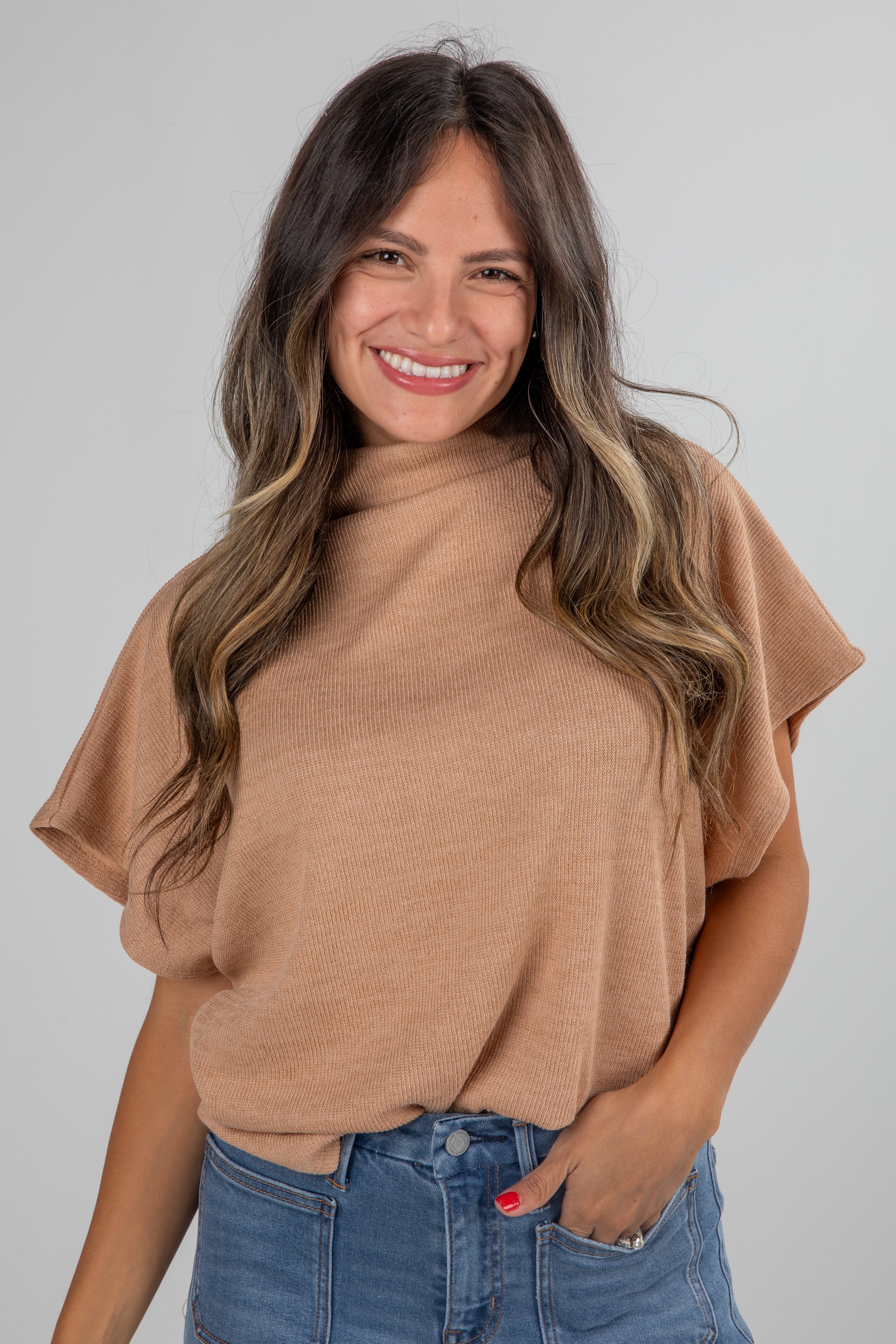 Woman wearing a tan sweater and blue jeans against a gray background