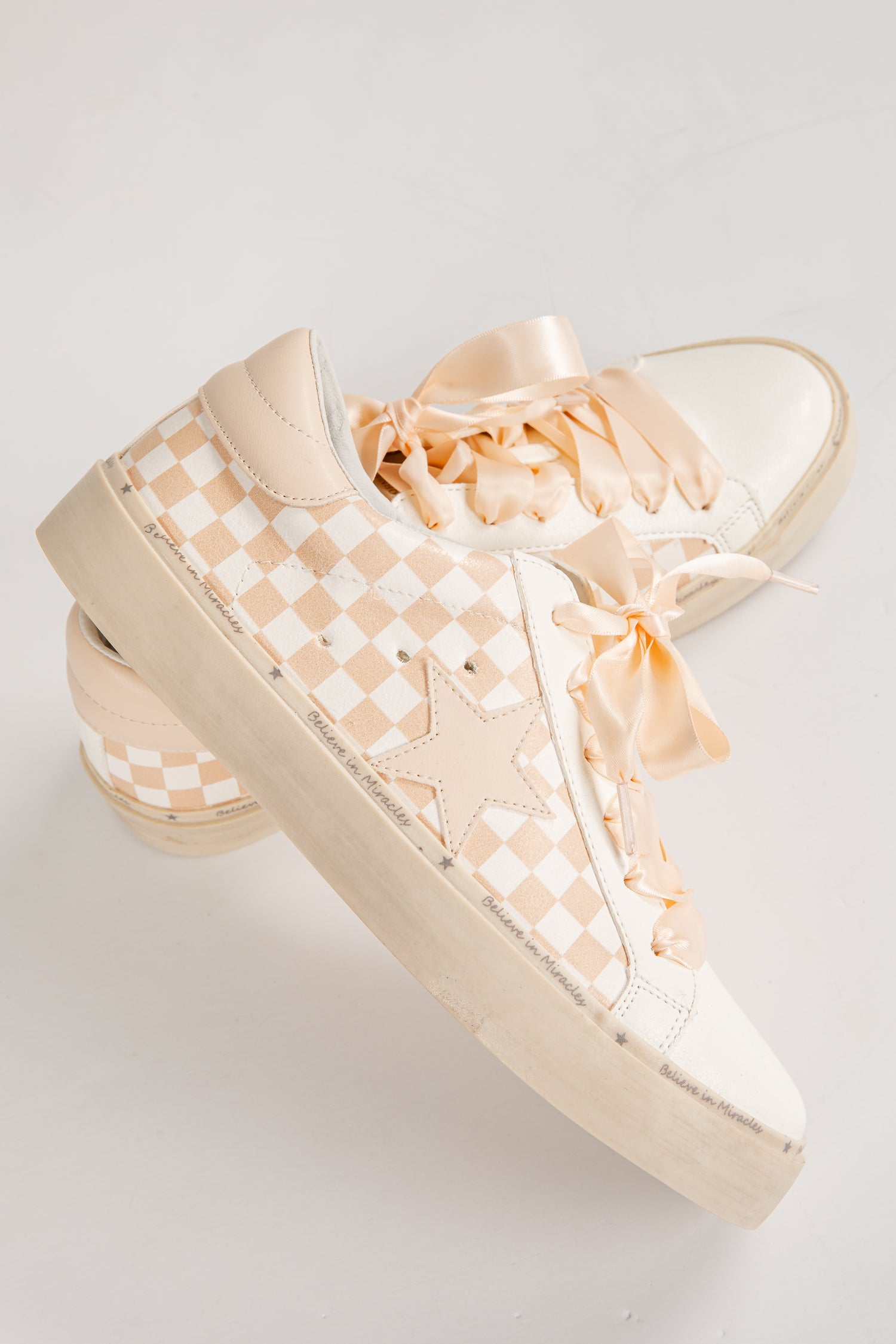 Beige checkered sneakers with ribbons on a light gray background