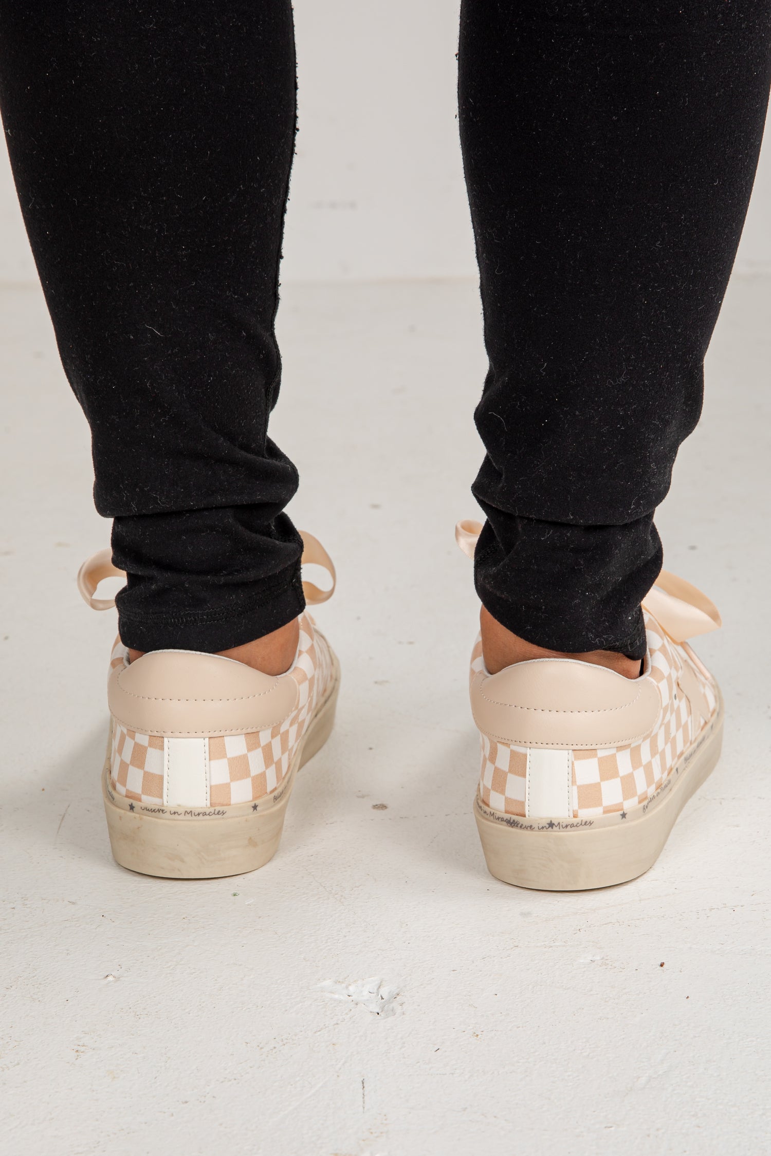 Person wearing checkered platform shoes with black pants on a light background
