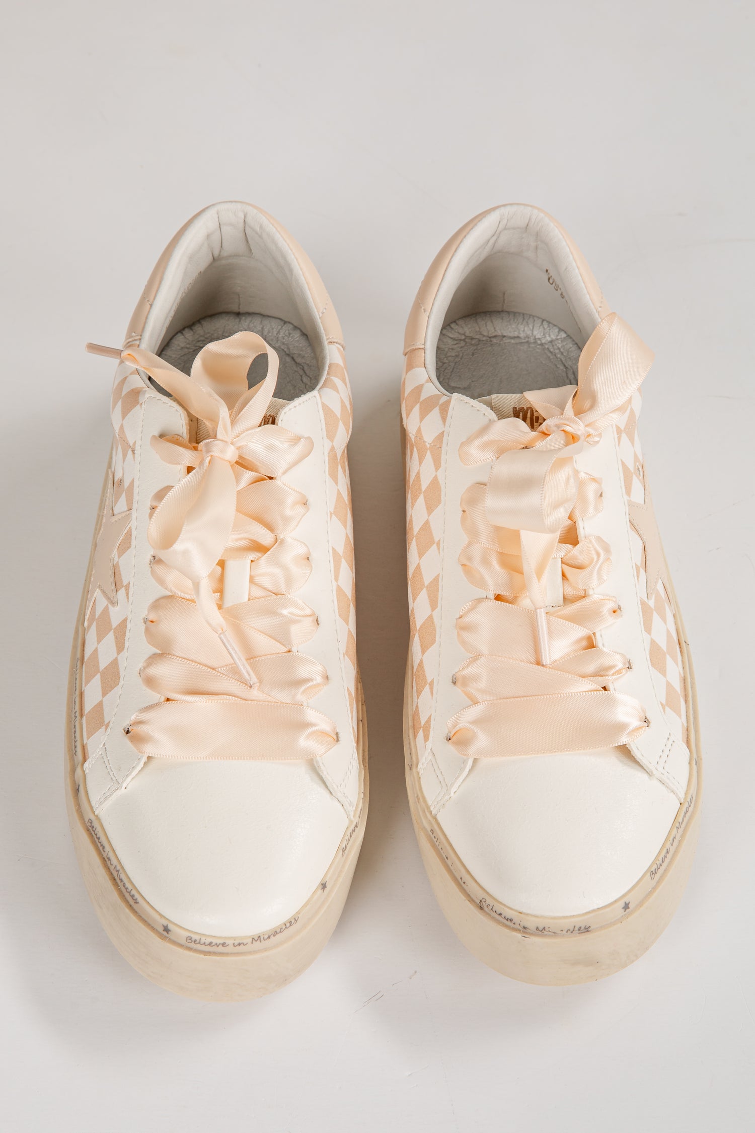 Pair of white sneakers with floral lace-up design on a light gray background