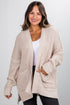 Woman wearing a beige chunky knit cardigan on a plain background