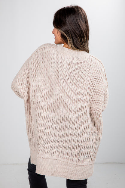 Woman wearing a beige knitted sweater against a white background