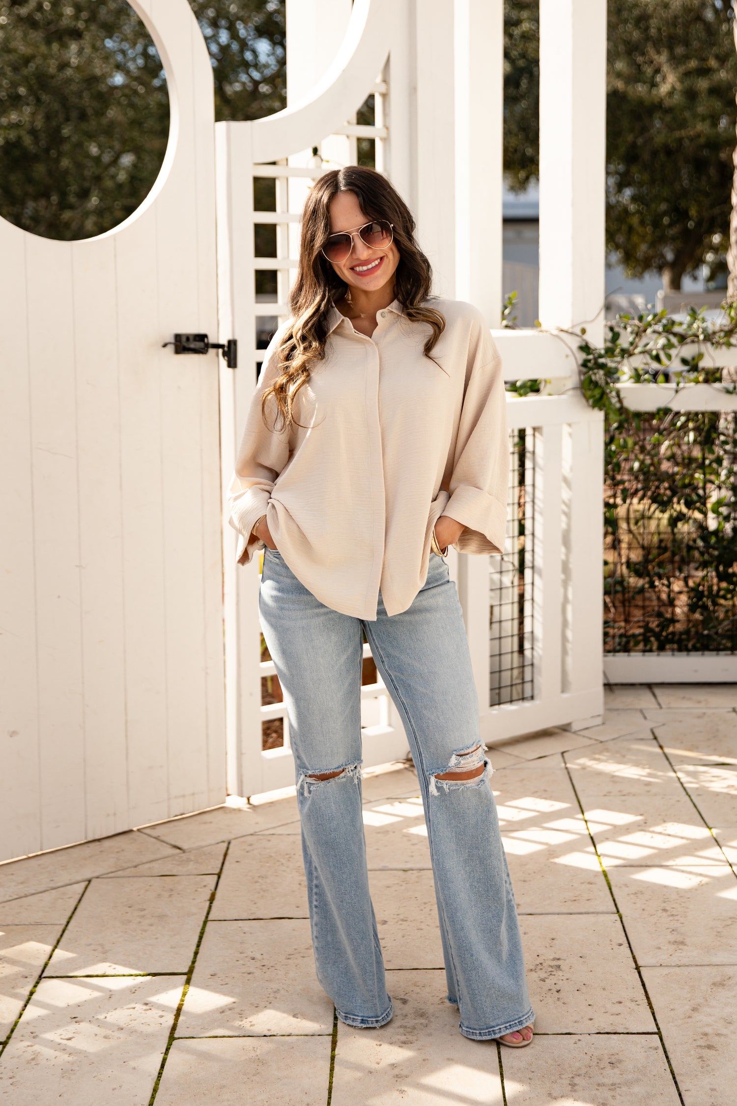 Woman in a beige jacket and light blue jeans standing on a patio.