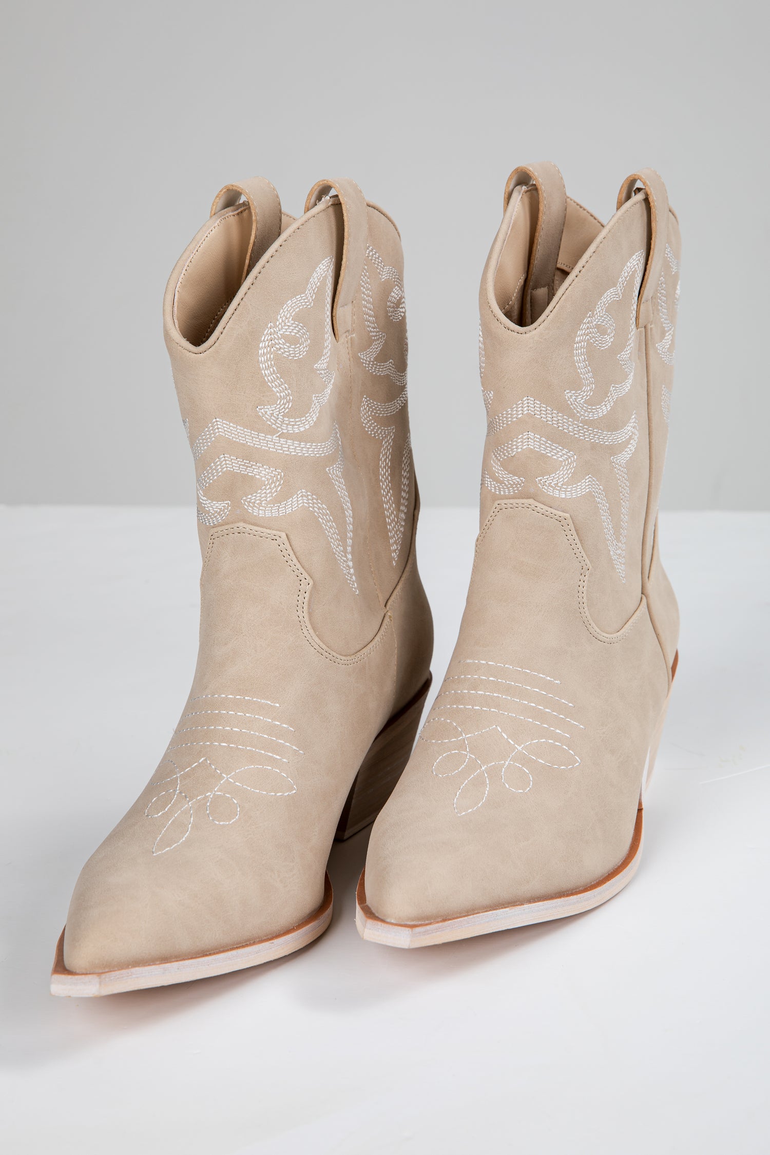 Pair of beige cowboy boots with white embroidery on a light gray background