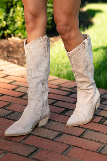 White cowboy boots on a person standing on a brick path with grass in the background