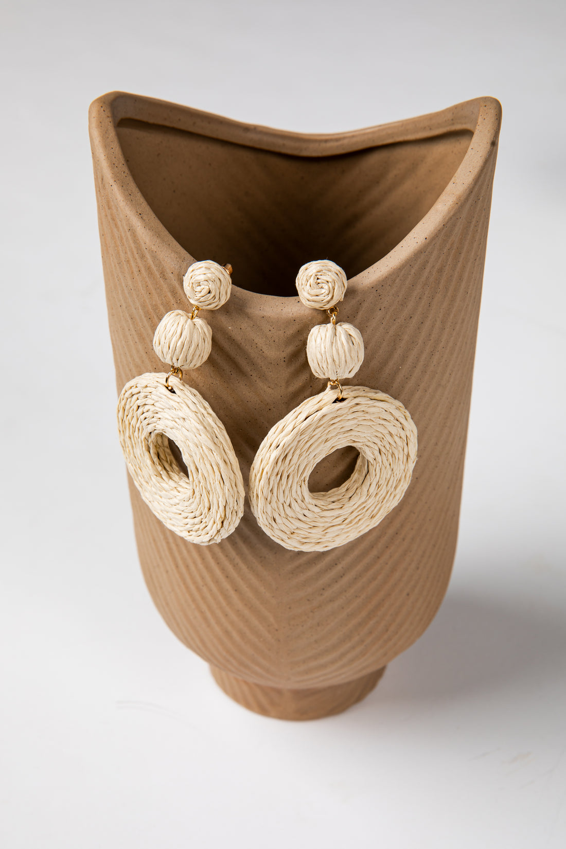 Brown woven vase with beige circular earrings on a white background