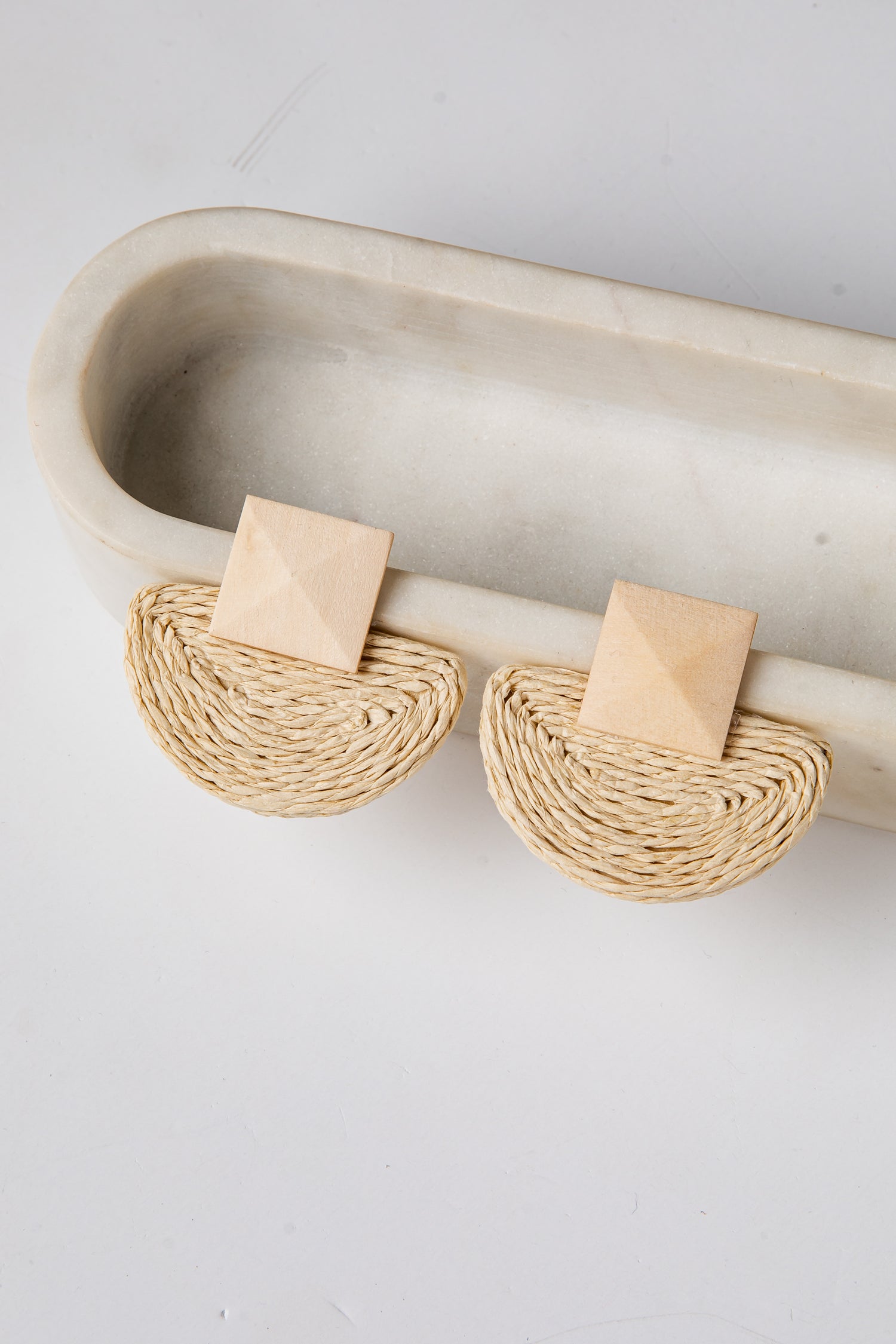 Pair of beige earrings on a white tray with a light gray background
