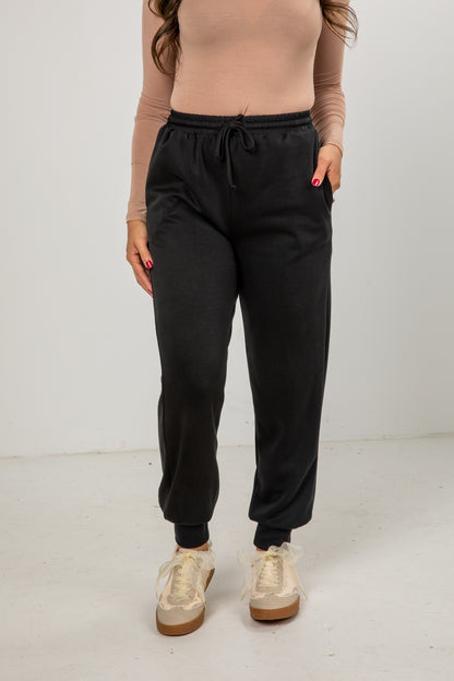 Person wearing black jogger pants and beige sneakers on a white background