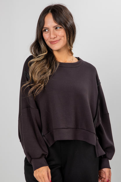 Woman wearing a dark brown oversized sweatshirt against a plain background