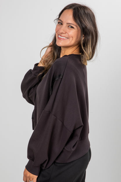 Woman wearing a dark brown oversized sweater against a plain background
