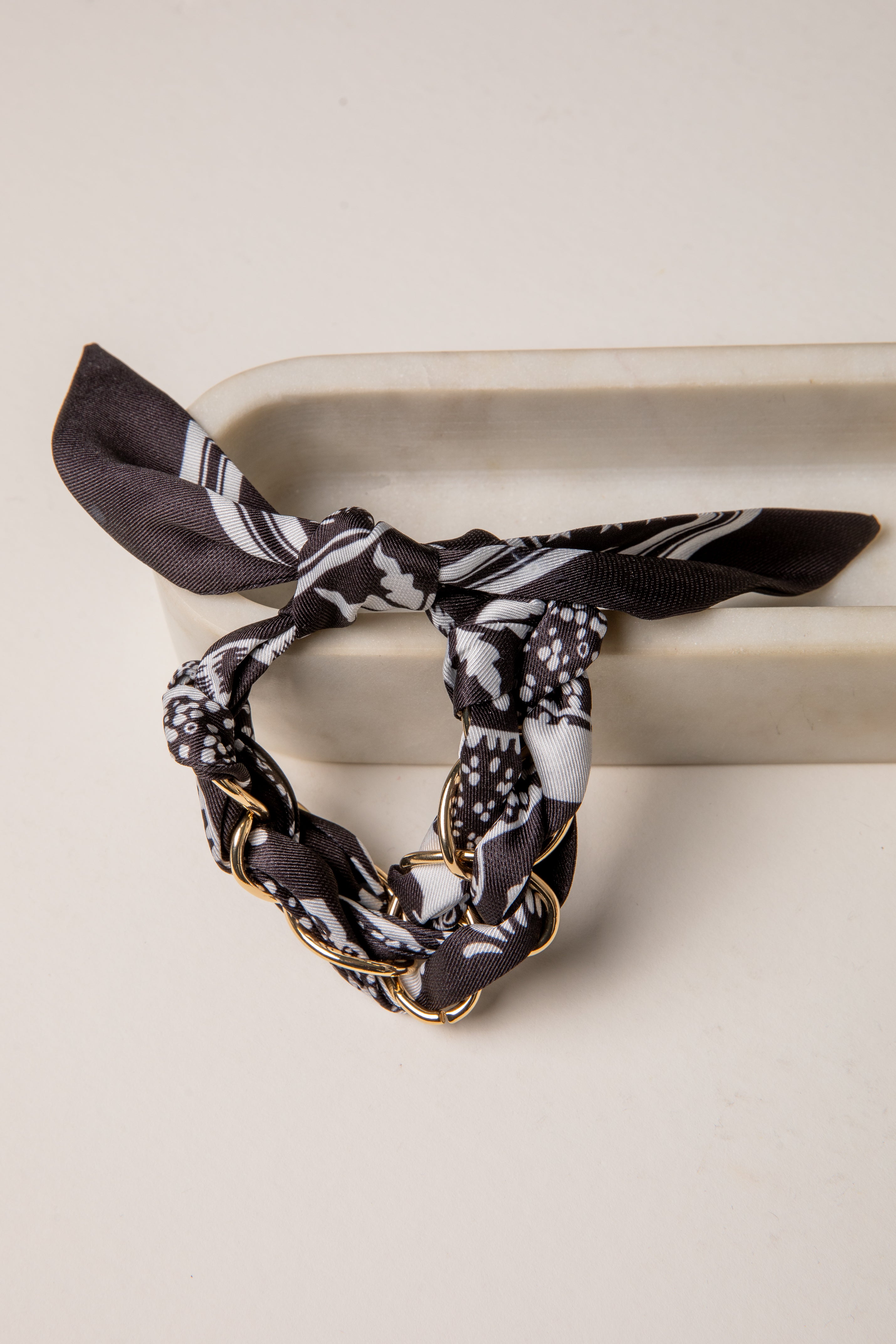 Black and white patterned hair scarf with gold chain on a beige surface