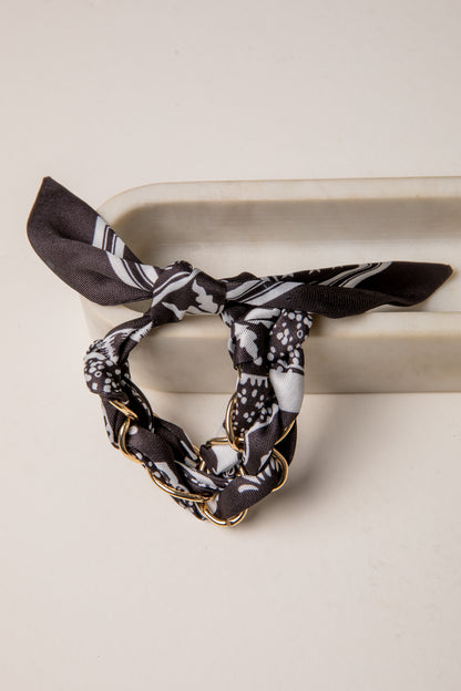 Black and white patterned hair scarf with gold chain on a beige surface