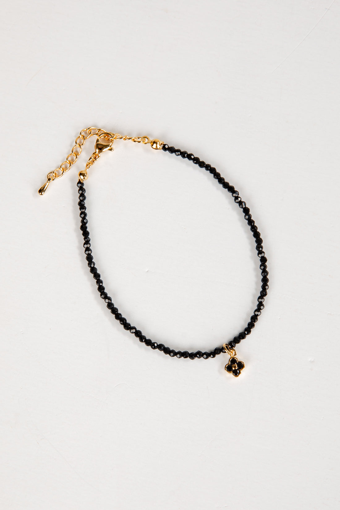 Black beaded anklet with gold chain on a white background