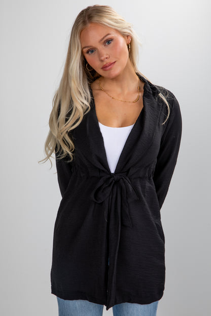 Woman wearing a black cardigan over a white top and blue jeans on a plain background