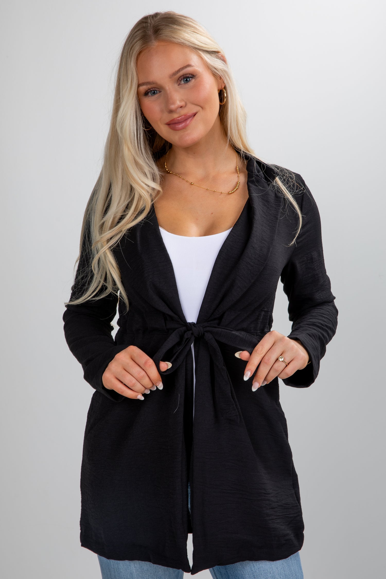 Woman wearing a black jacket over a white top on a plain background