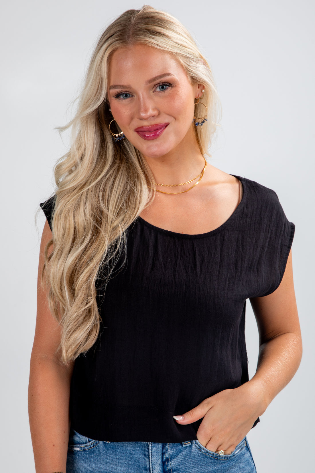 Woman wearing a black sleeveless top and blue jeans on a white background